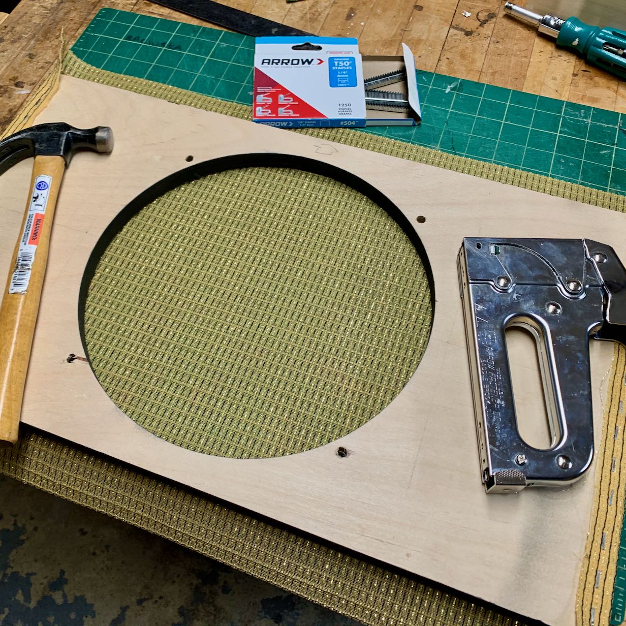 Build process photo showing gold striped fabric being stapled to the speaker baffle