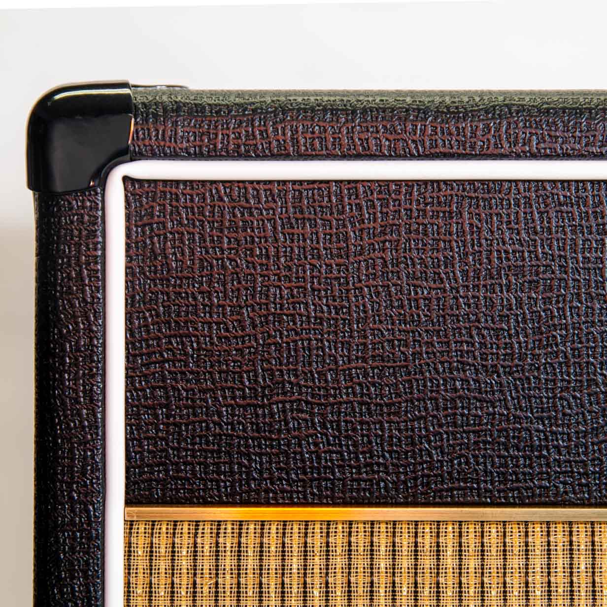 Cropped detail view of front top corner of amp showing textured vinyll, brass accent, and gold grill cloth